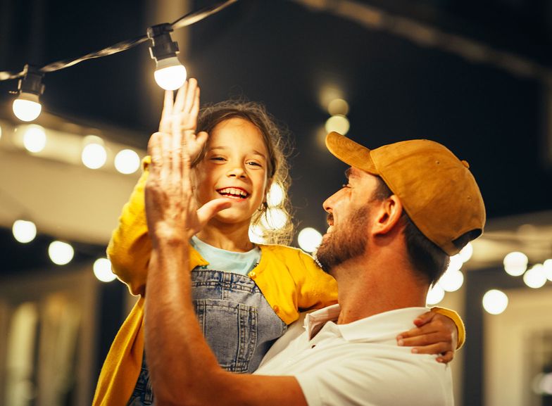 Father and daughter high five after fixing a string of lights in the backyard.