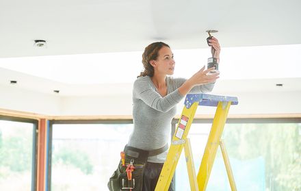 A woman standing on a ladder installing a lightbulb.