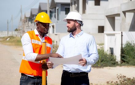 Two contractors meeting outside reviewing plans.