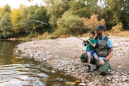 A father and son fishing along a rocky shore.