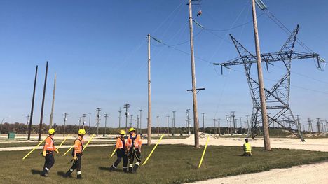 Les membres d’une équipe de monteurs de lignes sous tension effectuent des réparations, suspendus à un hélicoptère