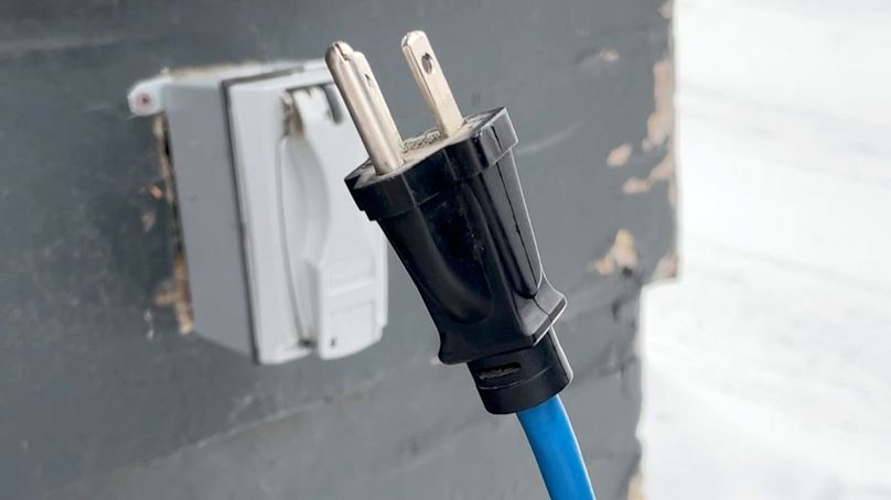 A photo of an outdoor extension cord in front of an outdoor electrical outlet.