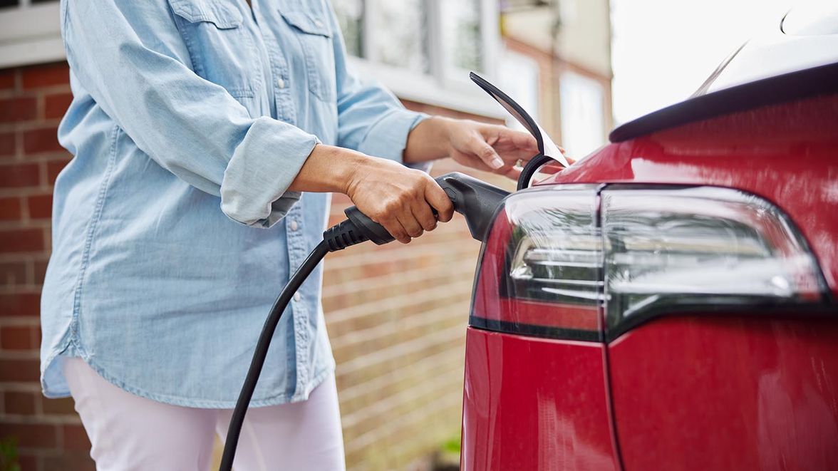 Close up of the rear end of a red car with an EV charging cable being plugged in by a person.