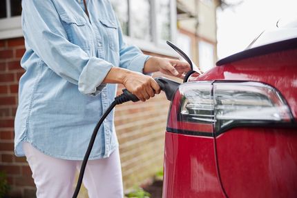 Close up of the rear end of a red car with an EV charging cable being plugged in by a person.