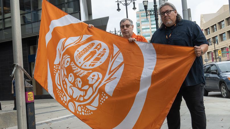 Deux employés de Manitoba Hydro se tiennent ensemble, tenant le drapeau des survivants avant qu’il ne soit hissé sur le mât à l’extérieur de Manitoba Hydro Place.