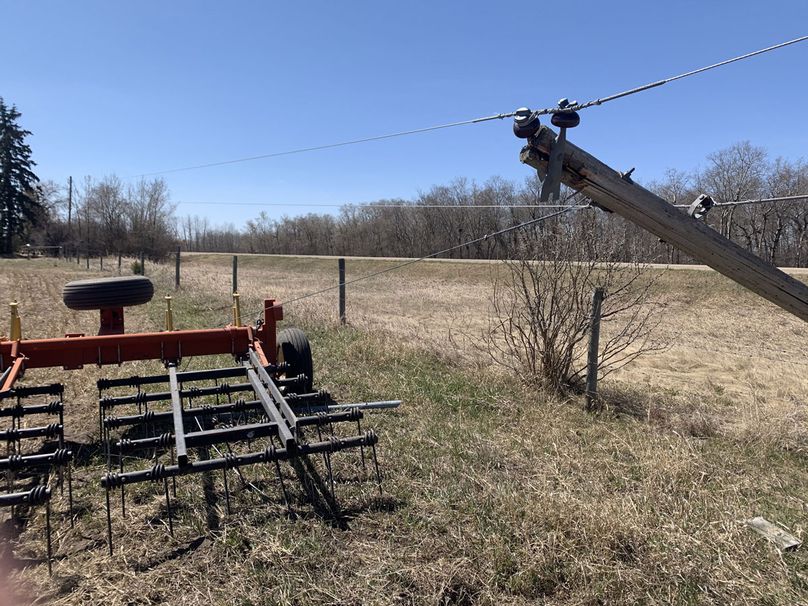 Farm machinery tangled with guy wire from a hydro pole.