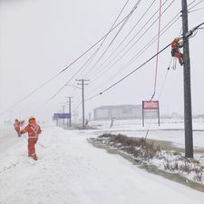 Des personnes en tenue de haute visibilité marchent à côté d’un poteau électrique et y grimpent.