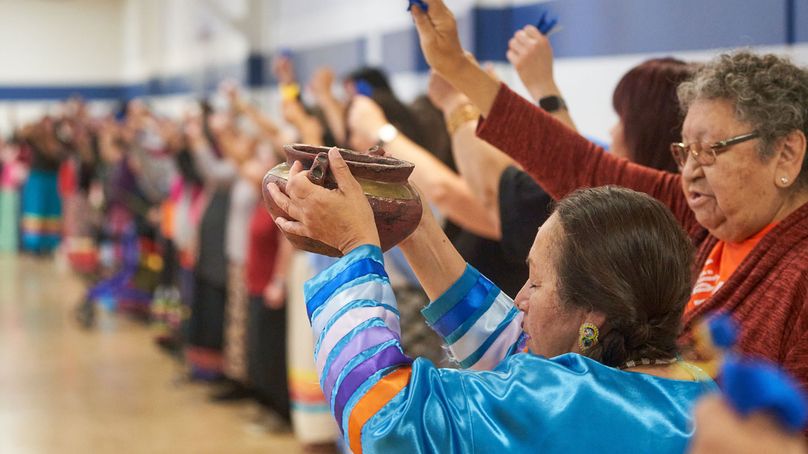 Woman leading the water ceremony holds up vessel of water as participants pray in each of the four directions.