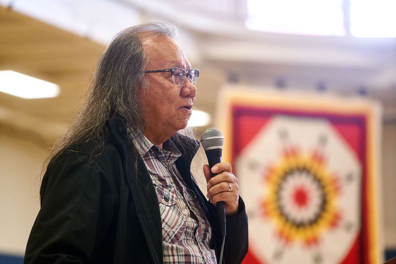 The emcee, with a traditional blanket hung in the background, speaks to everyone gathered.