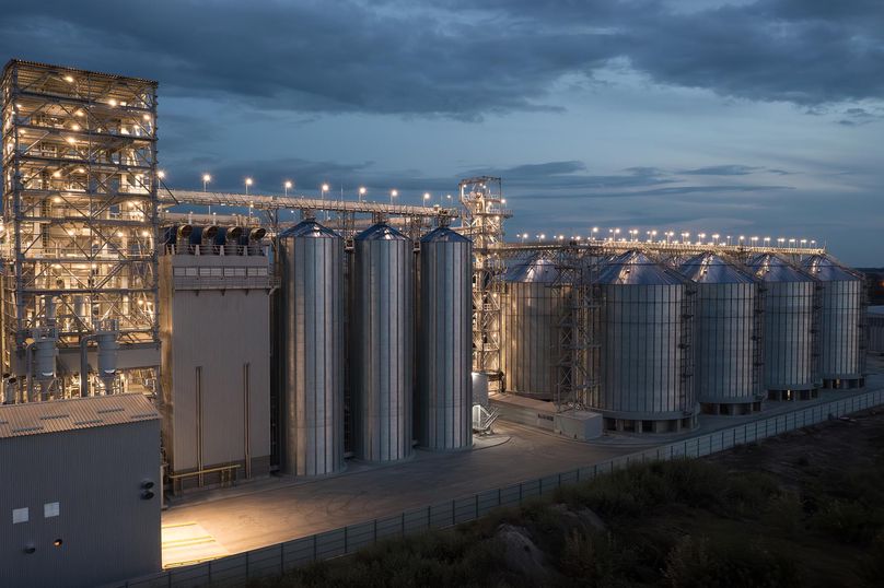 Une opération industrielle à grande échelle avec des lumières incandescentes et un ciel nuageux en arrière-plan au crépuscule.