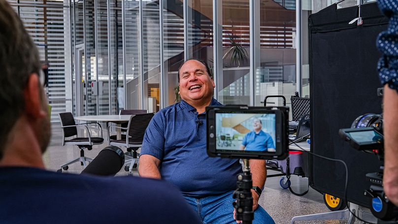 A man laughs while being interviewed on camera.