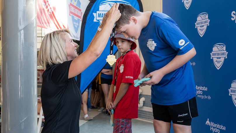 A Manitoba Hydro employee presents a gold medal to an athlete.