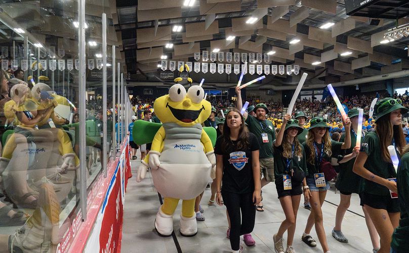 Athletes and coaches hold glowsticks and walk through a crowded arena. Louie the Lightning bug walks with them.