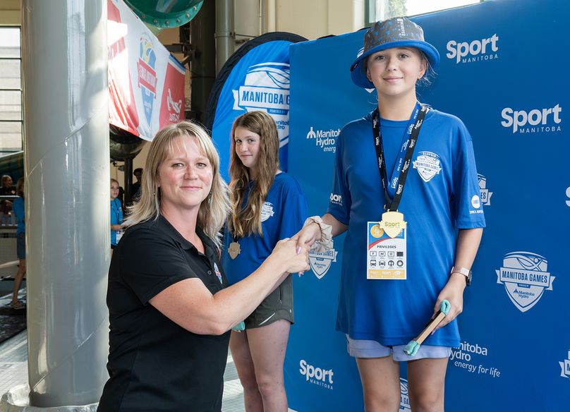 A Manitoba Hydro employee shakes hands with an athlete wearing a gold medal at the medal presentation.