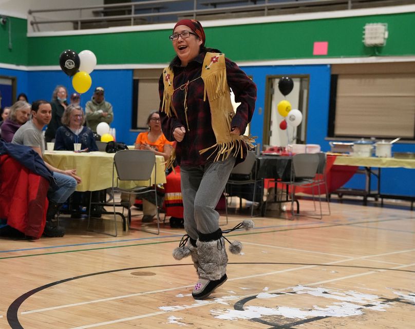 Individual in plaid shirt with leather beaded vest raises one foot in air.