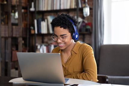 Une personne avec des écouteurs est assise à une table et travaille sur un ordinateur portable.