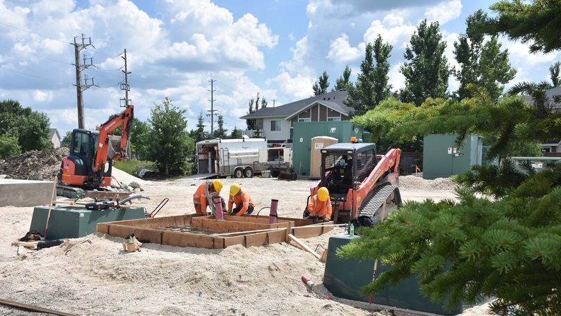 Trois personnes en vêtements à haute visibilité travaillent sur un socle en bois pour un transformateur sur un terrain en gravier.