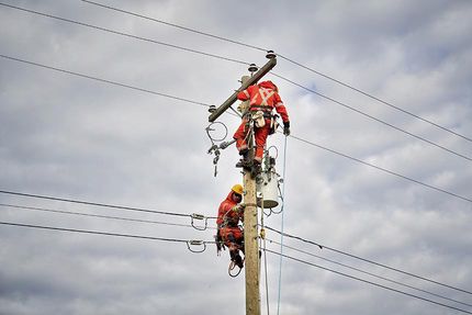 Deux techniciens de lignes électriques travaillant à réparer les lignes d’un poteau hydroélectrique.