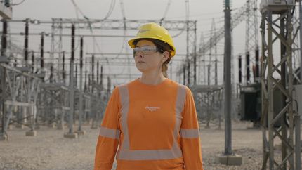 Manitoba Hydro employee wearing high-visibility safety equipment stands in front of a converter station.