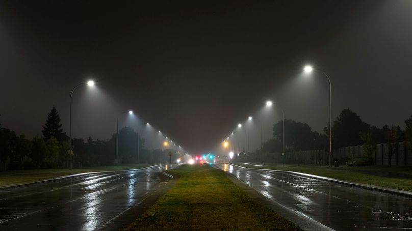 Une route faiblement éclairée et humide la nuit avec plusieurs lampadaires éclairant les deux côtés de la rue.