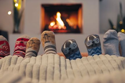 A photo of children's sock feet sticking out of a blanket with holiday-themed prints. A cozy fireplace is out of focus in the background.