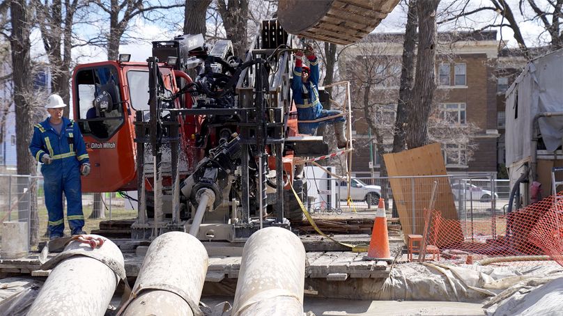 Three contractors wearing safety equipment operate a large boring machine.