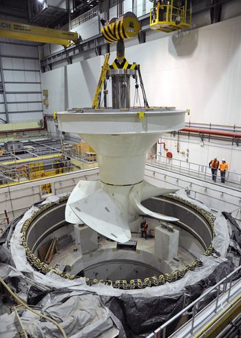 Travailleurs vêtus de casques protecteurs abaissant une géante turbine pour la mettre en place.