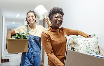 Two women carrying boxes and excited to move.